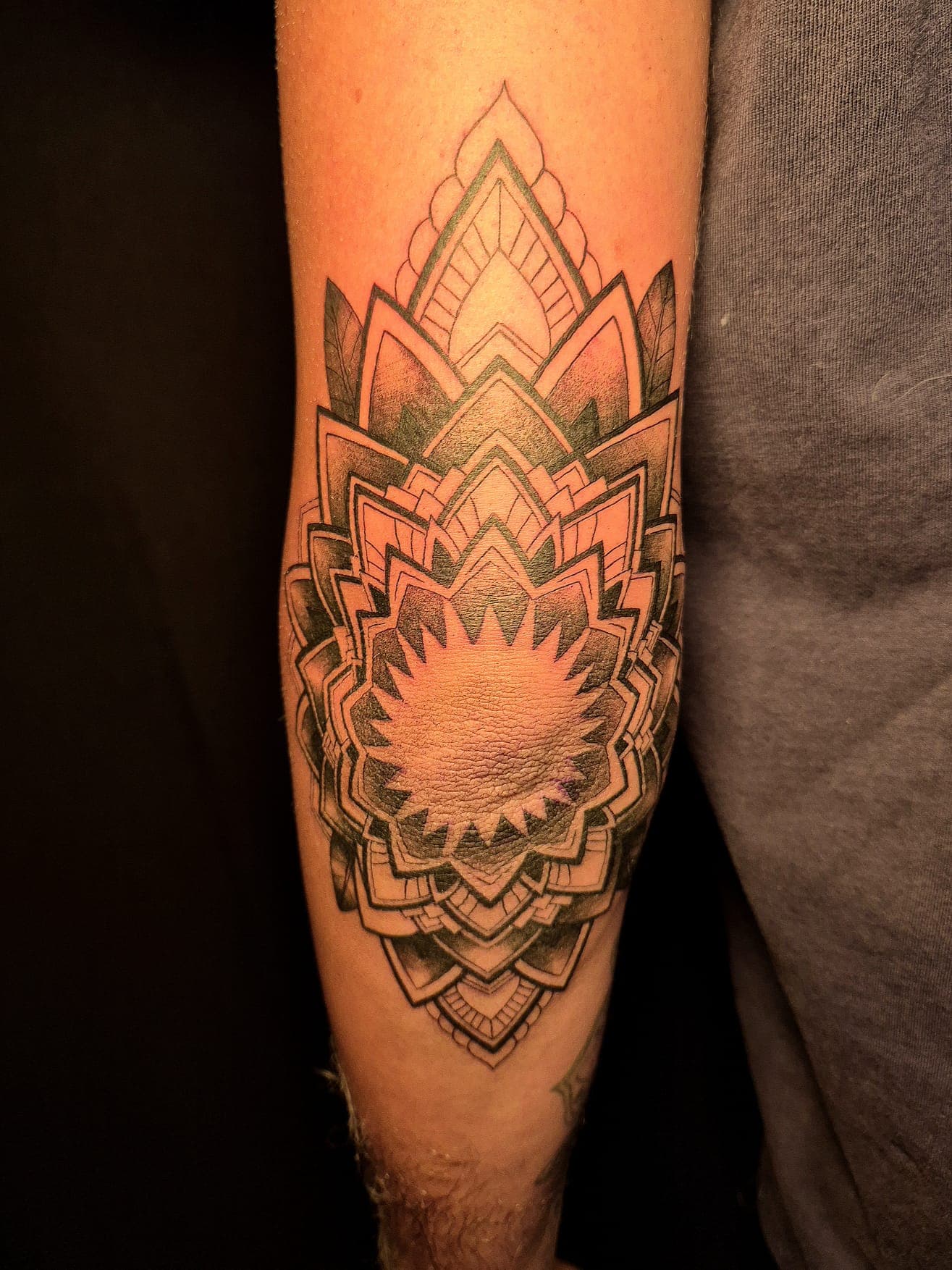 Mandala ornemental en noir et gris tatoué autour du coude, travail en dotwork
